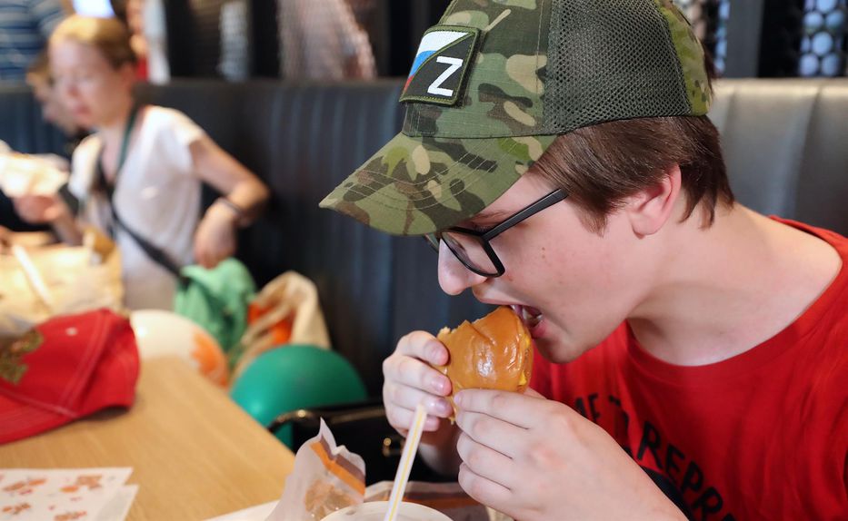 Joven ruso come en el nuevo y nacionalizado restaurant de comida rápida, luciendo un gorro con el símbolo 